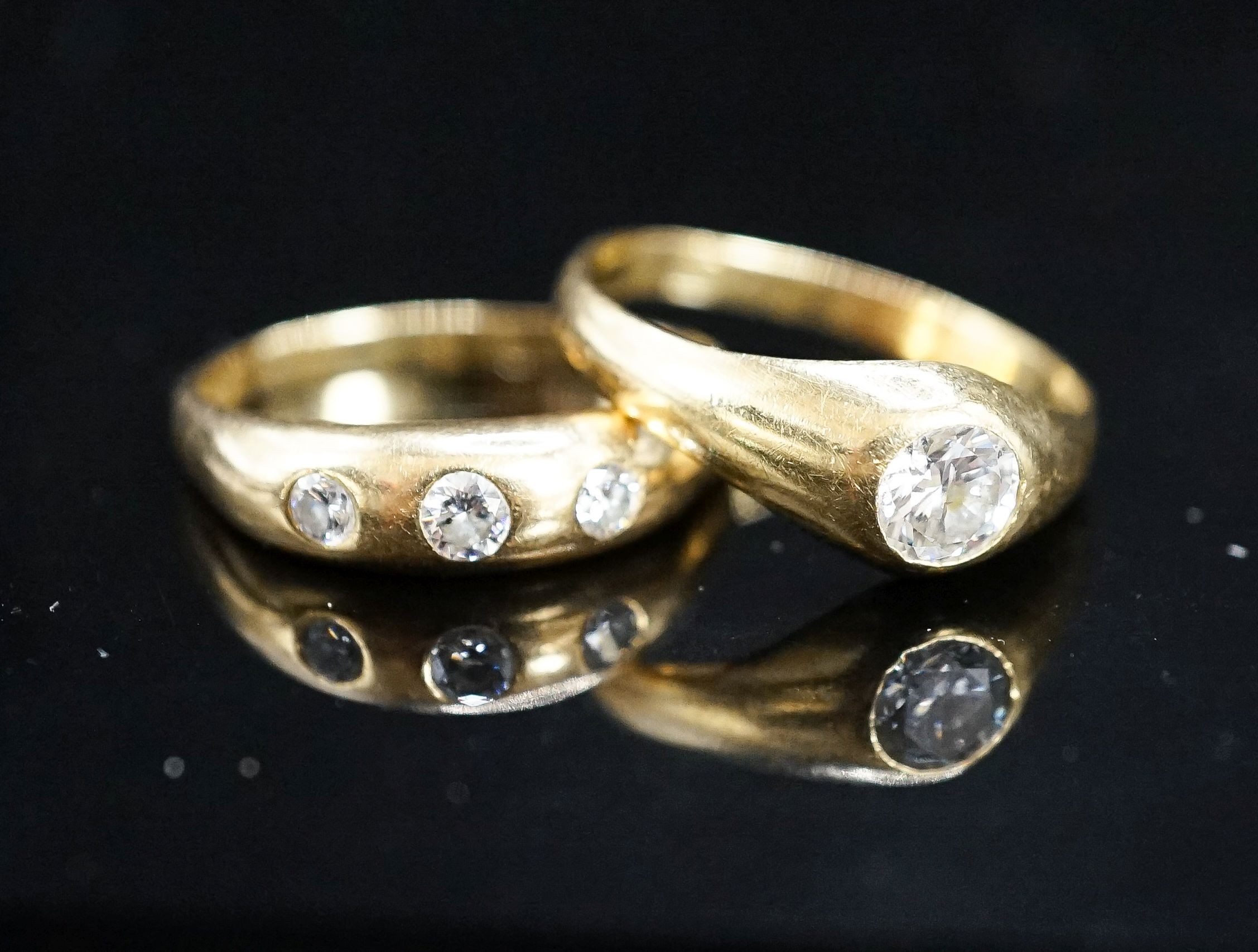 A modern 18ct gold and gypsy set solitaire diamond ring, size X and a similar three stone diamond ring (shank cut), gross weight 9.2 grams.